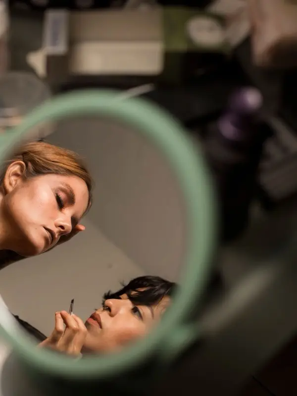 A makeup artist working on a client — seen through the mirror