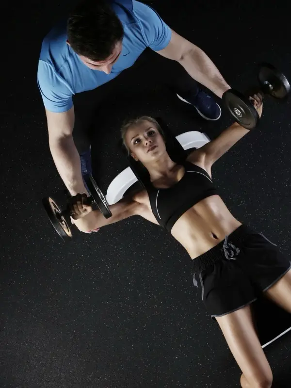 A trainer spotting a client during a dumbbell exercise