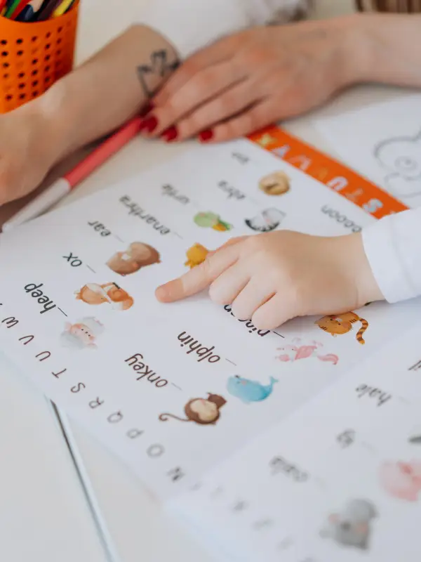 A child pointing at a picture in an alphabet sheet next to an adult's hand during a session