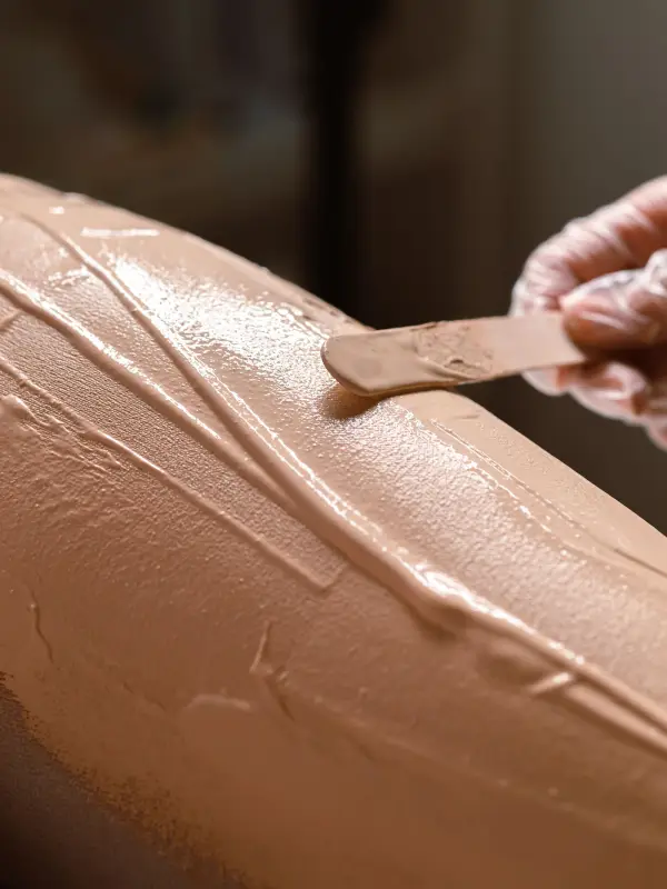 A specialist spreads sugaring paste on a client’s leg with a spatula, faces out of frame